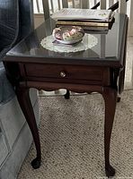 Full view of table beside sofa showing drawer, cabriole legs, glass top