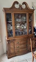 Full view of assembled china cabinet and hutch showing wood finish, three drawers, two doors, glass upper section