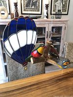 Stained glass balloon hanging next to painted bird mobile on dining background