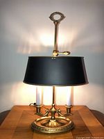 Front view of brass Bouillotte lamp illuminated with adjustable black tole shade