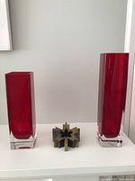 Both ruby red glass vases with maple leaf paperweight between