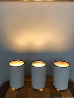 Three white cylindrical metal lamps lit and displayed on surface