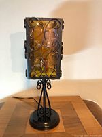 Full view of lamp showing wrought iron frame, amber acrylic shade, pedestal base