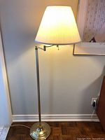 Full view of brass swing arm floor lamp with shade illuminated