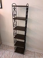 Full view of tall metal shelf showing five faux wood shelves and scrollwork sides