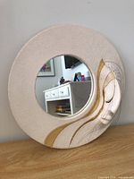 Front view of round ceramic mirror with sculpted face and gold accents