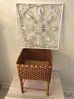 Overall view of wicker planter on stand with metal wall panel behind