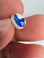 Close view of polished blue opal in white matrix held between fingers