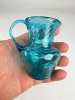 Front view of aqua blue hand blown glass pitcher held in hand