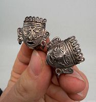 Front view of both Aztec mask earrings held between fingers