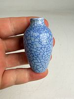 Miniature blue crackle-glazed vase held in hand showing overall shape and glaze