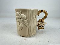 Full view of mug showing raccoon relief, tree-trunk body and sculpted handle