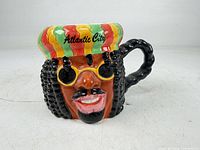 Front view of sculpted ceramic mug showing face, hat with Atlantic City text