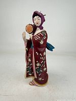 Front view of ceramic geisha figurine showing kimono details and hand drum