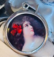 Front view of round sterling silver pendant showing painted portrait and bail