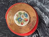 Top view of gold-tone compact showing engraved design and floral embroidery inset, red case beneath