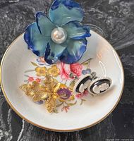 Dish showing floral pattern and gold rim with three jewelry pieces inside