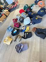Overall view of 22 assorted caps, visor and beanie laid out on floor