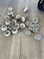 Assortment of 22 cabinet knobs on wood surface showing both ceramic and glass-topped styles