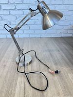 Full view of adjustable brushed metal desk lamp showing arm, shade, base and cord