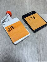 White Toshiba 2TB drive and black WD 1TB drive on wood surface