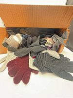 Open cardboard box filled with assorted knit gloves in multiple colours