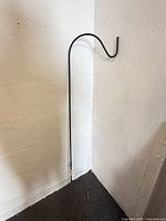 Full view of black metal shepherd’s hook leaning against wall