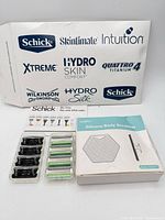 Lot overview showing Schick branded packaging sheet, two plastic holders with cartridges, boxed silicone scrubber