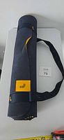 Rolled navy and yellow yoga mat standing upright with strap visible and logo patch
