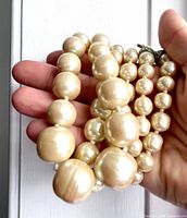 Hand holding graduated faux pearl strand showing size variation