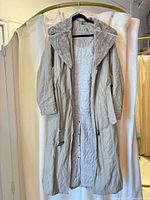 Front view of long beige parka hanging, showing overall style, faux fur collar and quilted lining