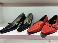 Black and red shoes side by side on shelf showing uppers and general condition