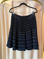 Front view of black pleated skirt hanging