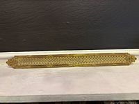 Full view of elongated gilt vent grille on white surface