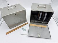 Two gray metal 8mm film storage cases, one open showing interior dividers and four reels