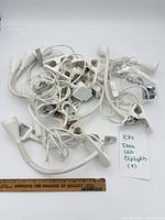 Pile of seven white IKEA LED clip lights with ruler for scale