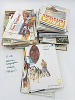 Stack of assorted National Geographic folded maps with Alaska map on top, handwritten note indicating 75+ maps