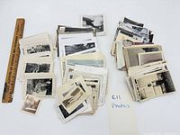 Overall view of multiple stacks of loose vintage snapshots beside ruler for scale
