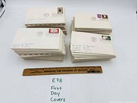 Four stacks of First Day Covers next to ruler and lot tag