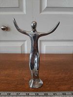Front view of polished aluminum Hoselton figure with arms raised, ruler showing height ~7.5 in.