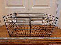 Full view of rectangular black metal wire basket on wood surface showing overall shape and grid design