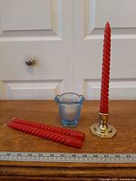 Group shot showing brass candlestick with red taper, blue glass votive and extra red tapers