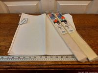 Two sealed packs of ivory Aida fabric alongside larger unrolled cloth and ruler for scale