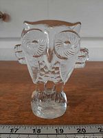 Front view of clear glass owl figurine showing spiral eyes and base with ruler for scale