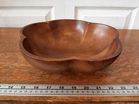 Oblique view of carved monkey pod wood bowl beside ruler for scale