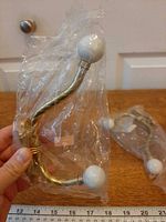 Hook held in hand showing brass twist, porcelain ends, packaging, ruler for scale