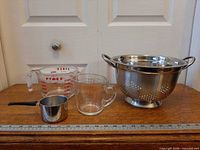 Lot overview showing colander and three measuring cups with ruler for scale
