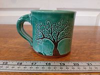 Profile of mug with Tree of Life design next to ruler