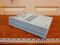 Stack of twelve light blue exercise books side view with ruler for scale
