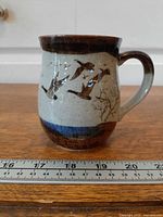 Front view showing flying geese artwork, brown rim, blue band, size reference